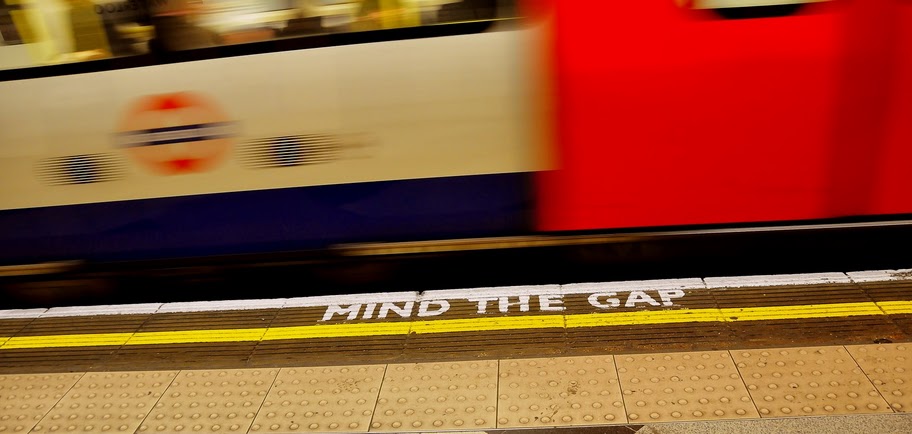 Train rushing by a platform with the painted words, “Mind the gap.”