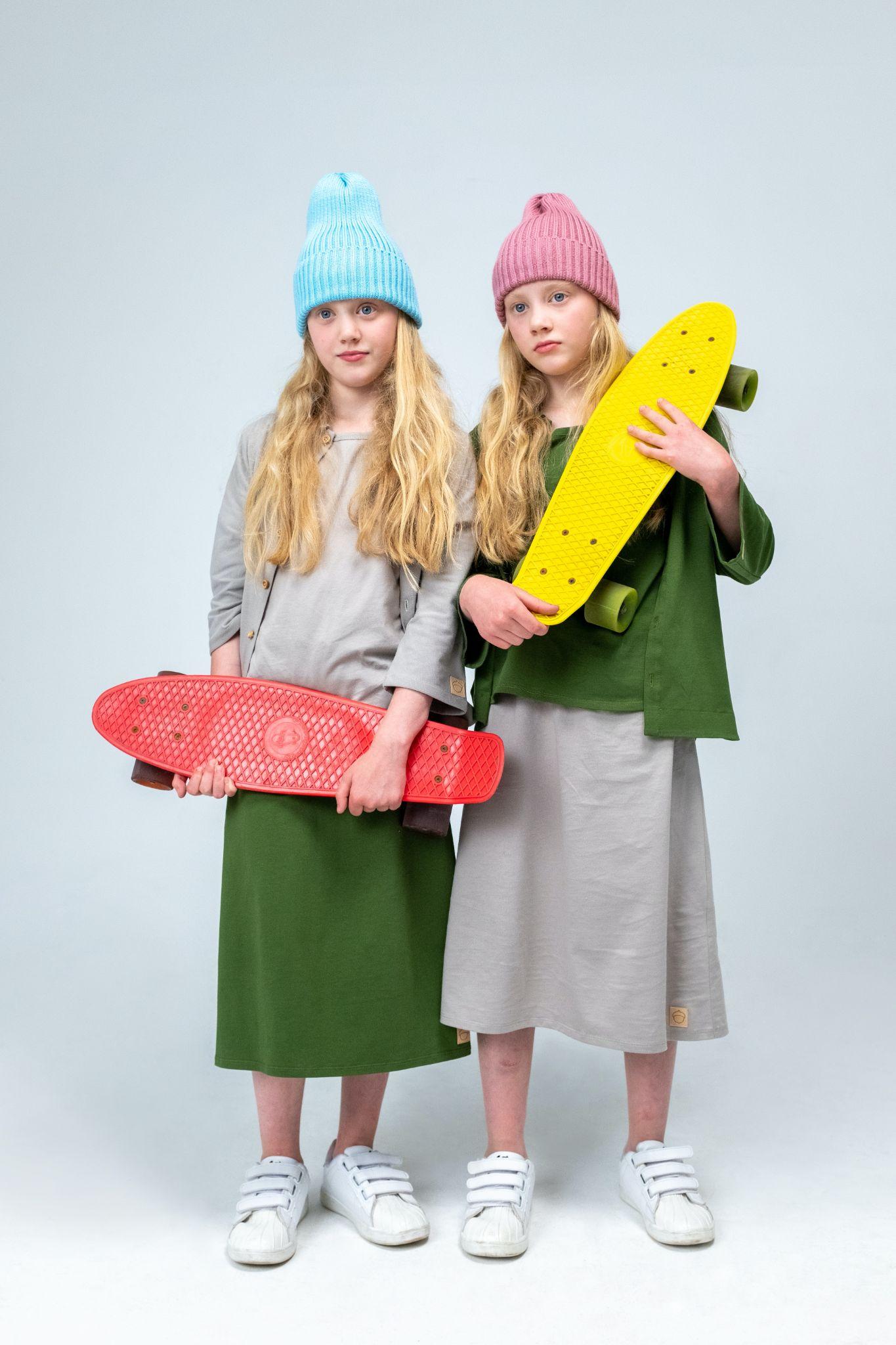Two girls, identical twins, who are both carrying skateboards and wearing knitted caps.
