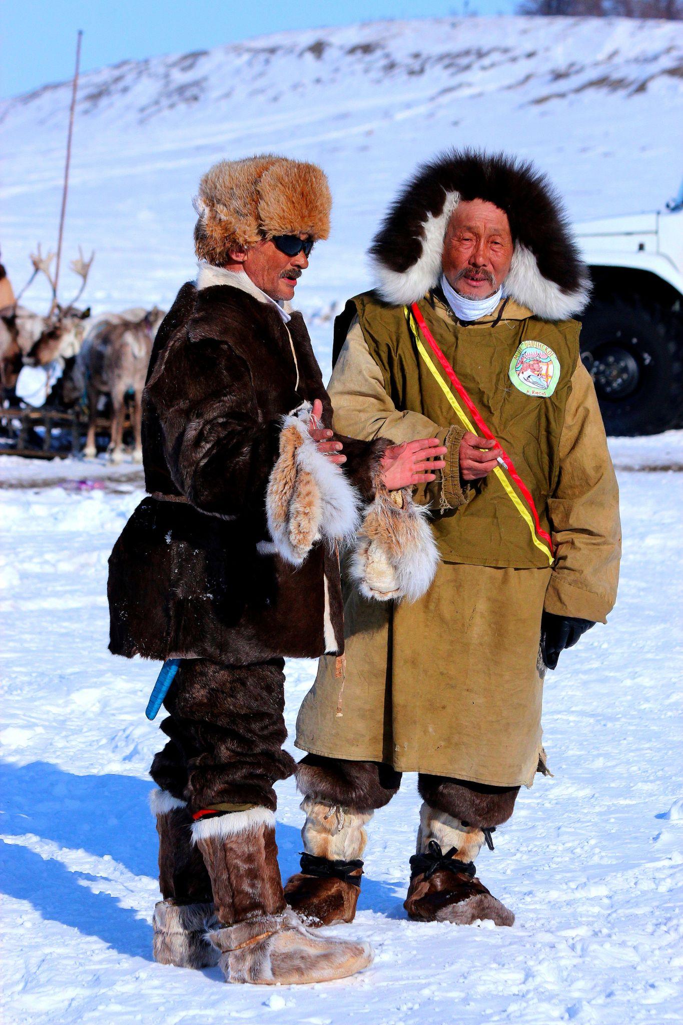 Two Inuit men in fur jackets standing on the snow.