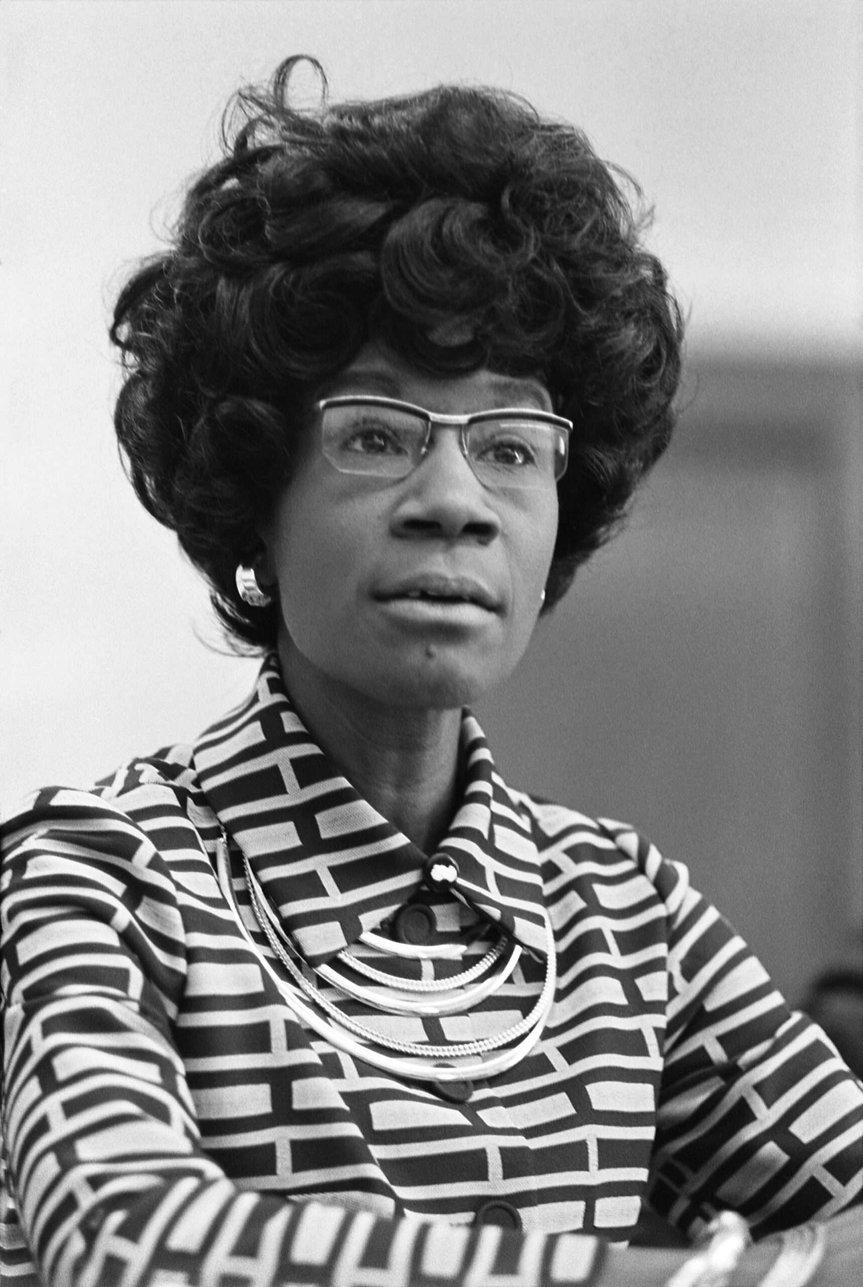 Photograph of Shirley Chisholm sitting at a press conference.