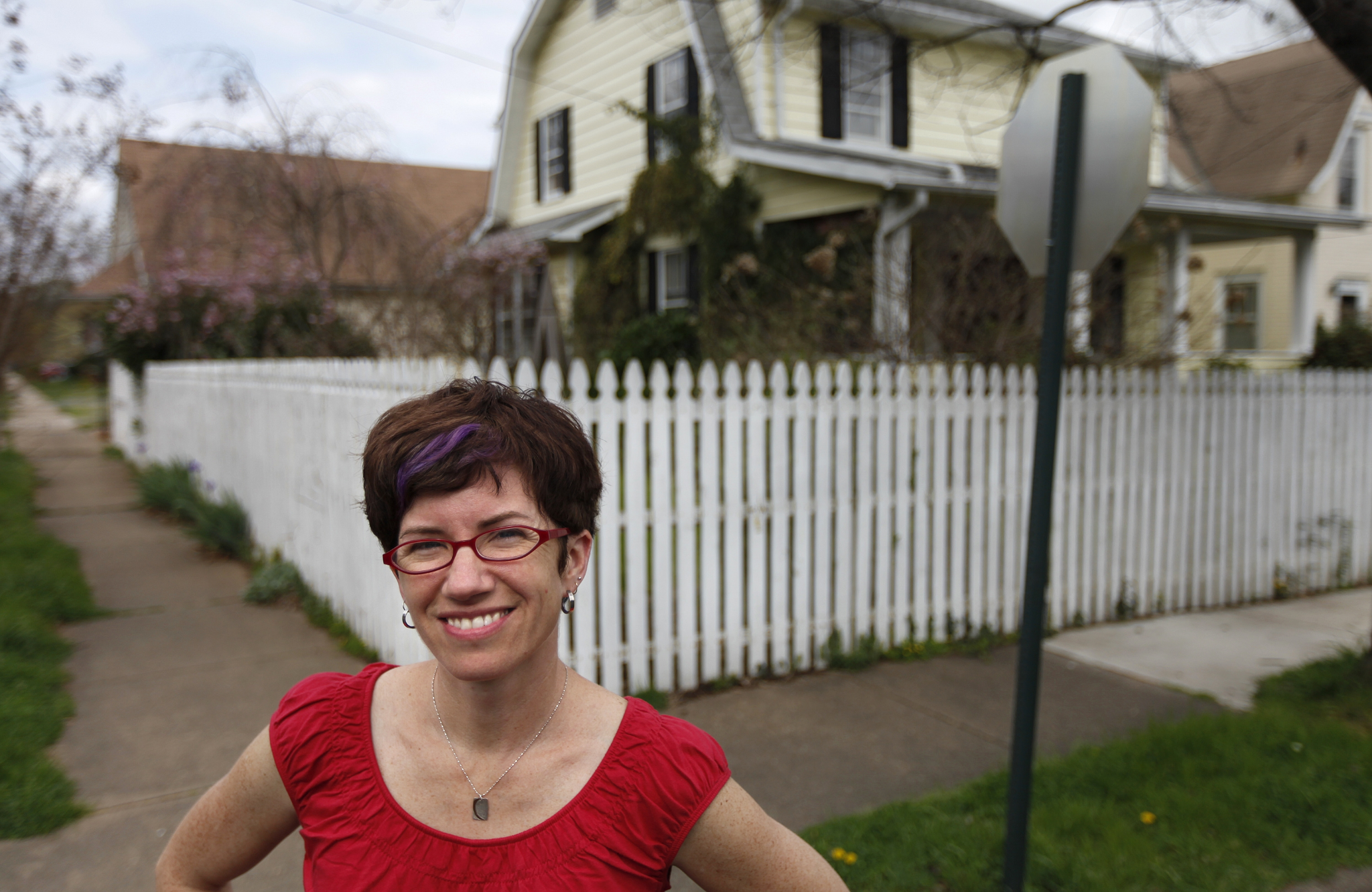 Photo of Leslie Martin standing on a suburban street corner in front of a white picket fence.