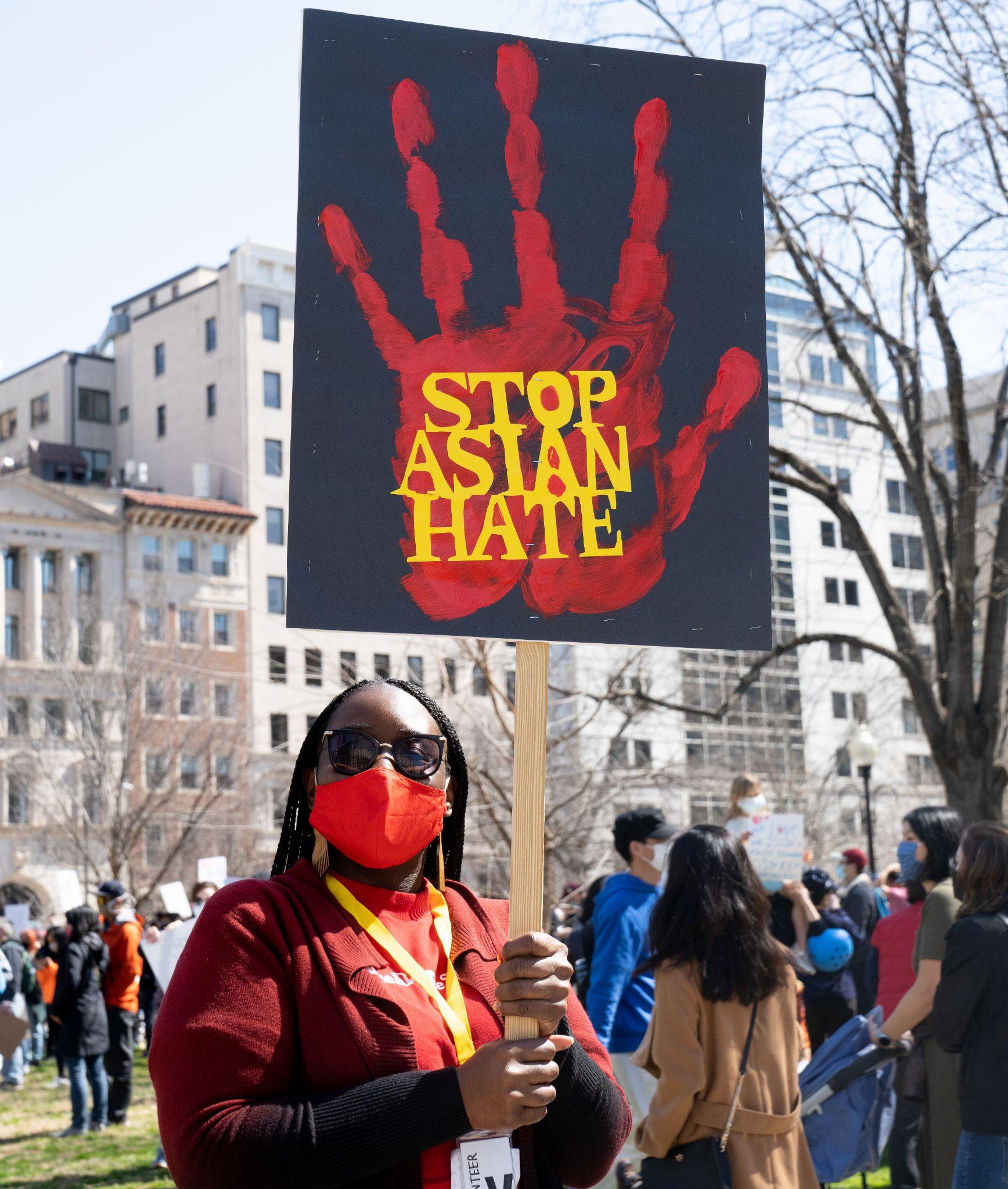 Woman at a rally wearing a mask and holding a sign that reads “Stop Asian Hate.”