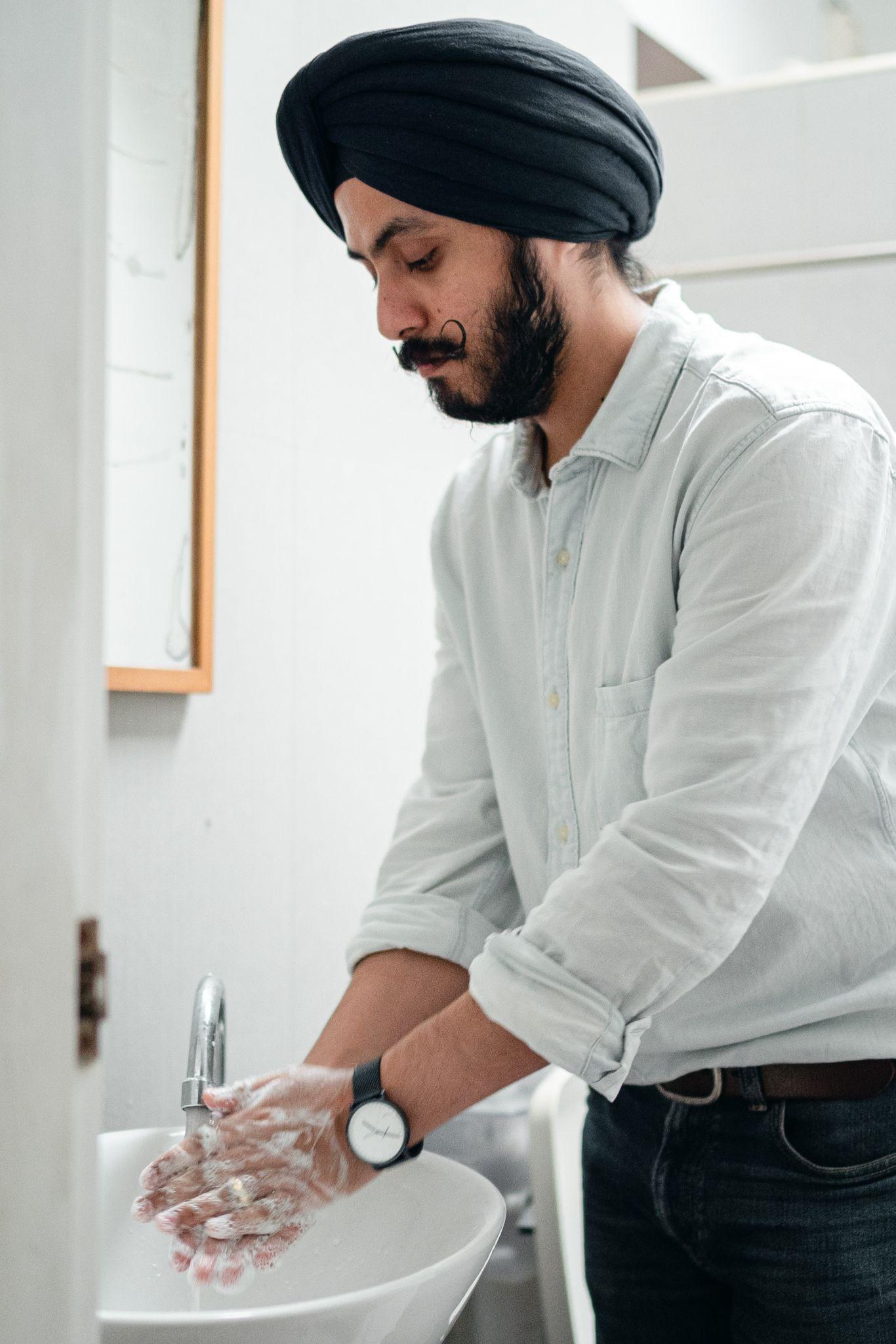 Man with a mustache, beard, and turban washing his hands at a sink.