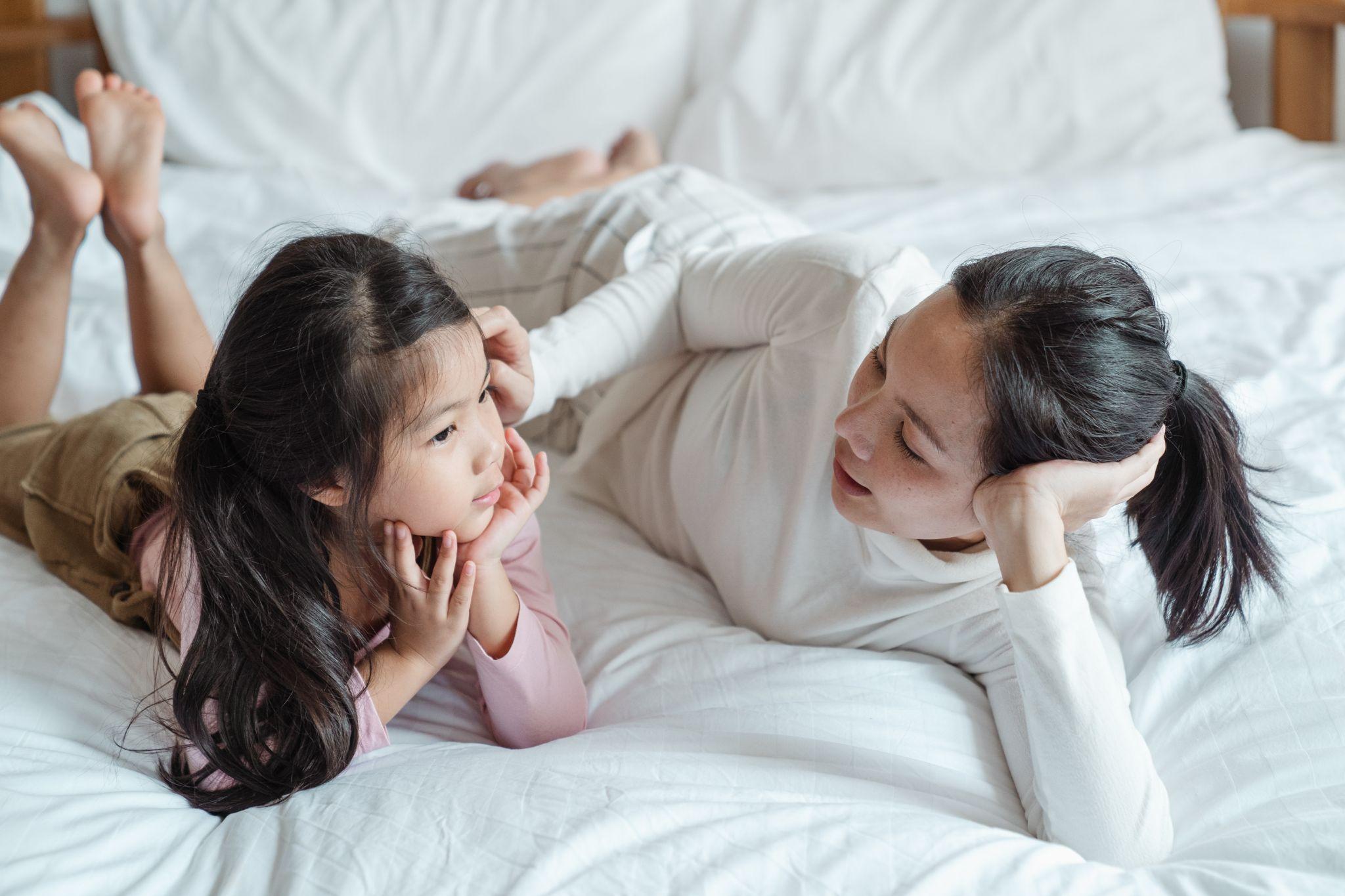 Woman talking to a young child while lying on a bed.