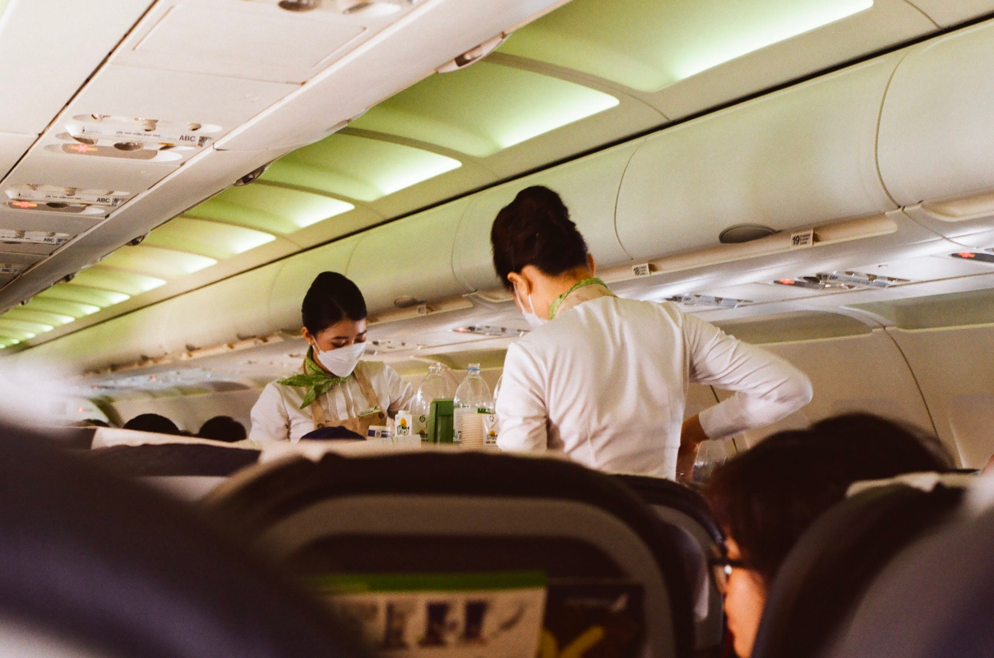 Flight attendants wearing face mask while standing on the aisle of an airplane.