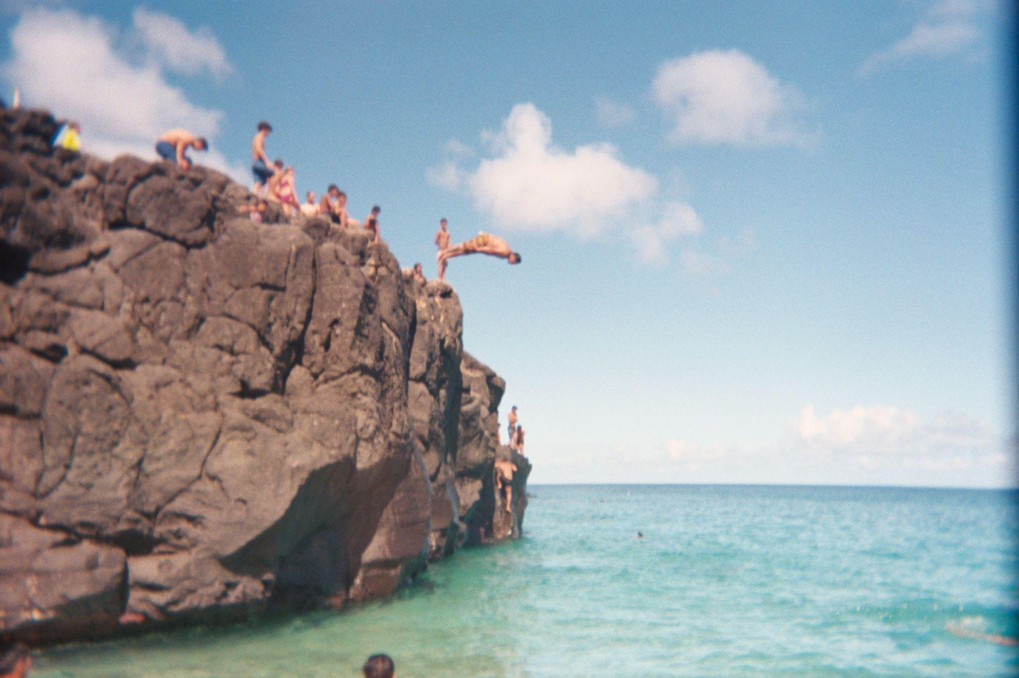 People jumping off a cliff into the ocean.