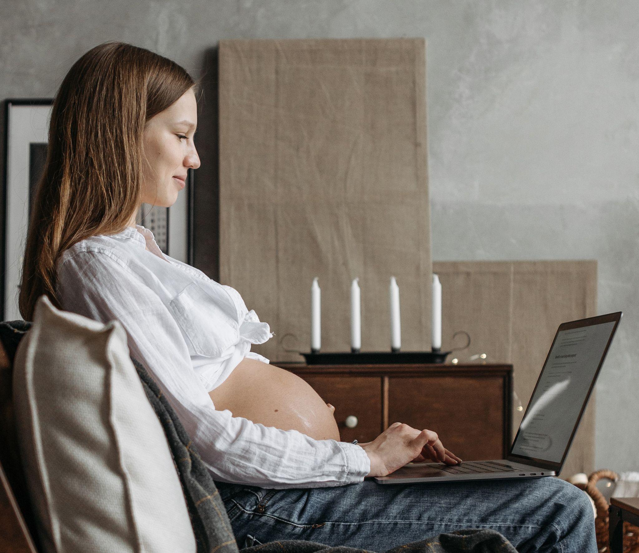 Picture of a pregnant woman sitting down with a laptop on her lap.