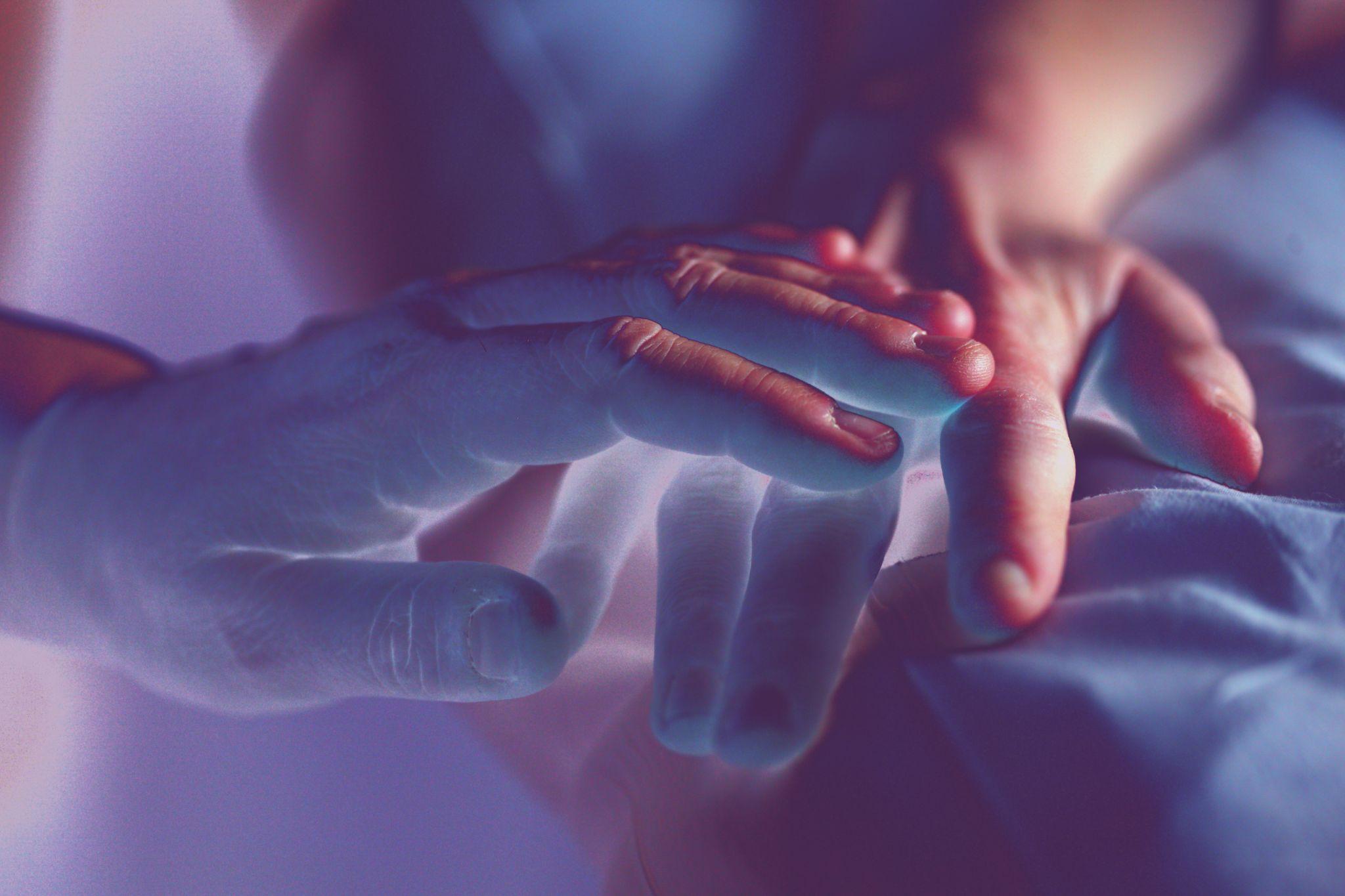 A person touching another person’s hand as they lie in a bed.