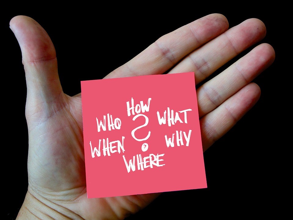 hand holding a post-it note that says "who, how, what, when, why, where"