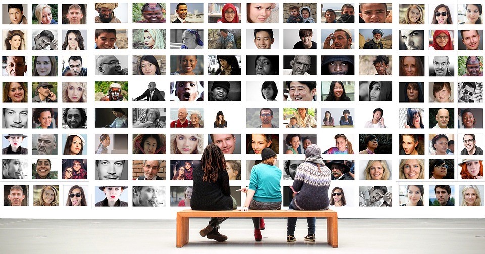 three people sitting on a bench in front of a wall composed of different people's photographs
