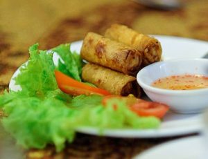 A plate of Chả giò, a traditional fried spring roll served in Vietnam. It is pictured on a plate next to dipping sauce and garnished with lettuce and tomato