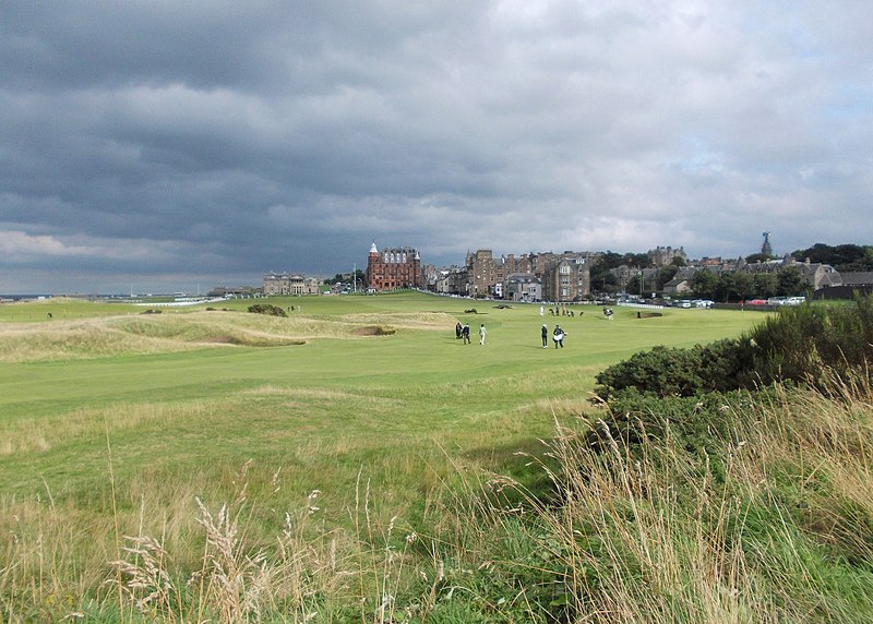 View of green grass on the golf course at St. Andrews, Scotland with distant players walking and storm clouds rolling in the distance