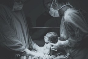 This image shows a baby being delivered via C-section by two doctors