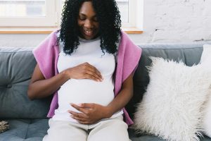 A pregnant woman sitting on a couch looking down at her belly