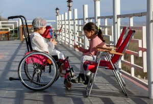 A child in a wheelchair and a child in a folding chair talking.