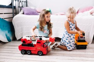 Two little girls playing together with toy trucks.