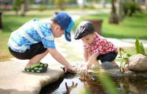 Two young children squatting down and playing with their hands in a pond