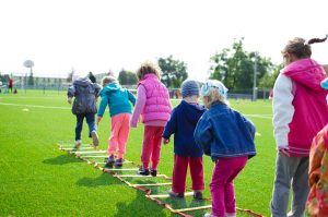 A group of children playing outside on an agility ladder.