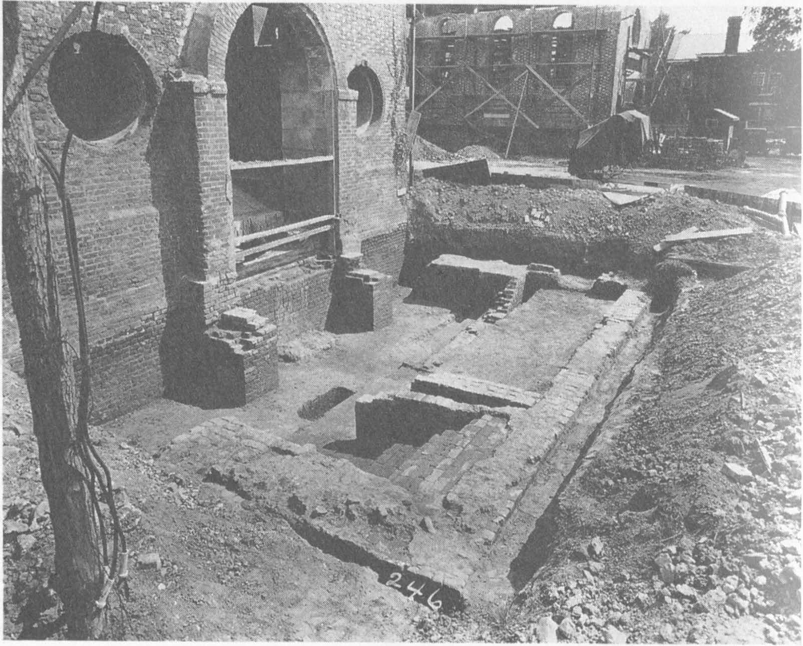 Excavation site revealing brick foundations and part of a building wall with circular openings and an arched doorway.
