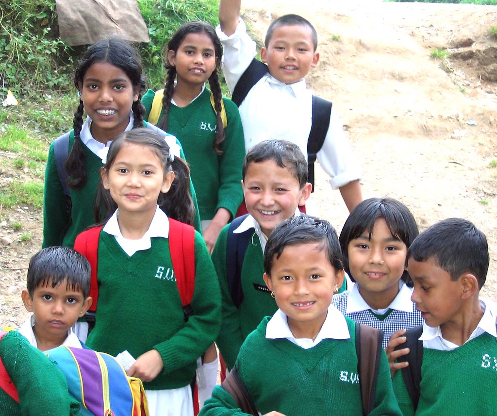 A group of elementary school-aged children in green uniforms standing together smiling.