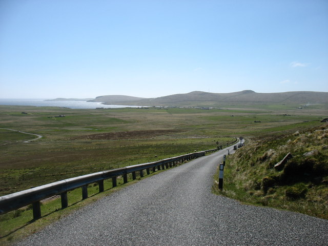 A winding country road in a flat, green landscape on a sunny day