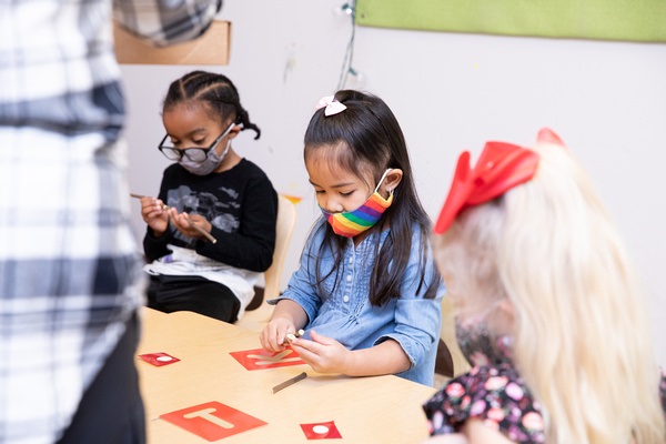 Children work at a table using stencils and sticks to explore letter formation.