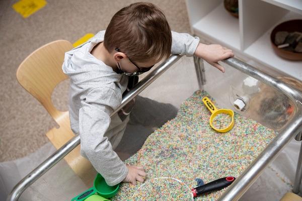 A child plays at a sensory table while seated.