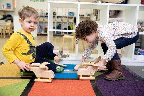 Two children play on the floor with block helicopters.