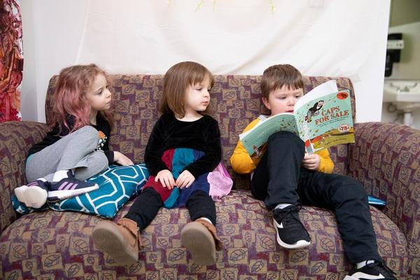 Three children read togehter on a couch.