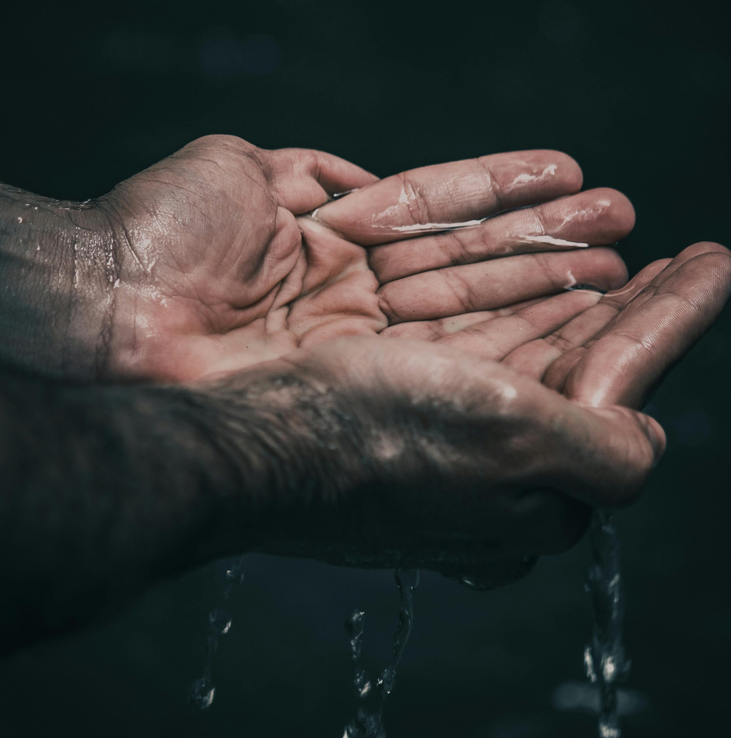 two hands cupped, holding water, but the water is dripping through the fingers below the hands.