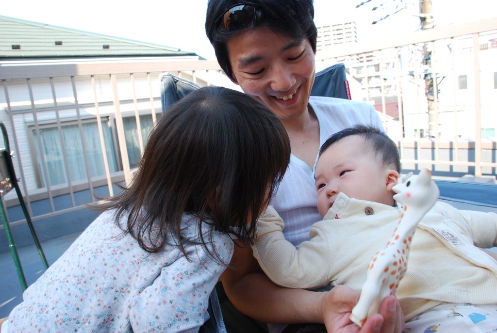 An Asian adult holding a baby, with another child in frame.