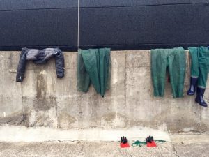 Four articles of clothing hanging on a wall and a pair of gloves at the base