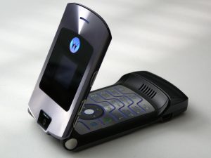 A cell phone, the original Motorola RAZR, sits on a white table flipped halfway open exposing numerical keypad.