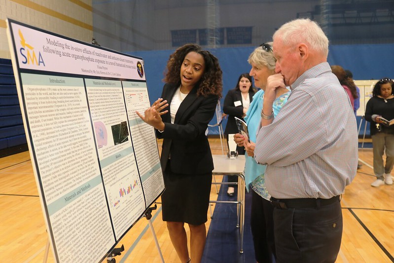 A student stands in front of a poster explaining it two two observers.